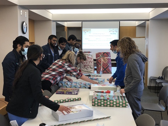 Group of people standing around a conference table and wrapping presents for the holidays